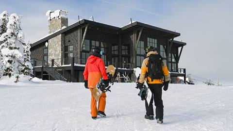 Two snowboarders walking up to Sky House