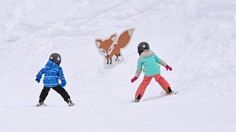 Two young skiers heading toward a cute carboard fox sign. 