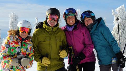 4 skiers with helmets smiling on a sunny day at Schweitzer. 