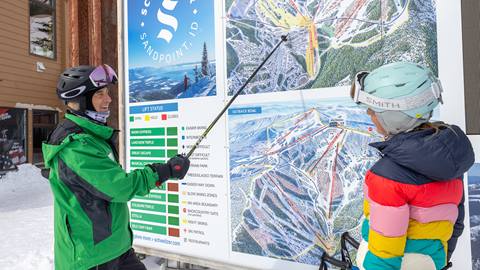 Mountain Host at Schweitzer pointing to a large map, showing a skier where to go next. 