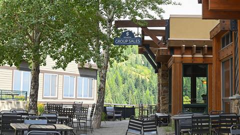 Exterior of the Schweitzer Group Sales office in summer with a logo sign, tables and chairs. 