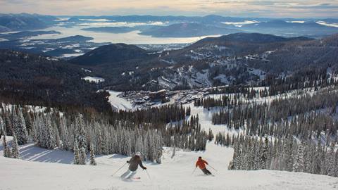 2 skiers at Schweitzer with a view of the Village and Sandpoint's Lake Pend Oreille