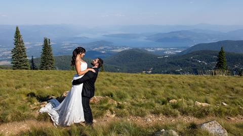 Bride being lifted up by her husband at the summit of Schweitzer and a view of Lake Pend Oreille