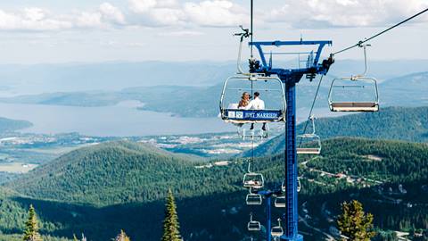 Newly weds on a chairlift with a stunning view of Lake Pend Oreille at Schweitzer with a sign saying just married. 