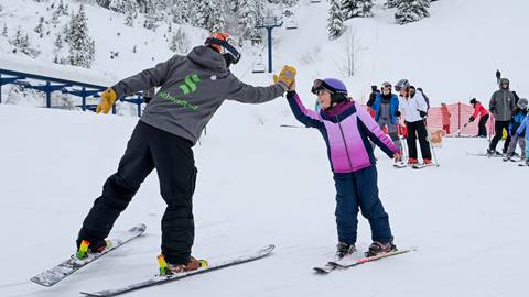 kid on skis high fiving ski instructor