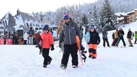 Snowboard instructor and group of kids with snowboards walking