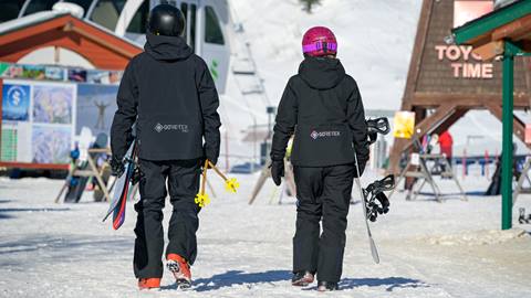 skier and snowboarder walking in village with equipment