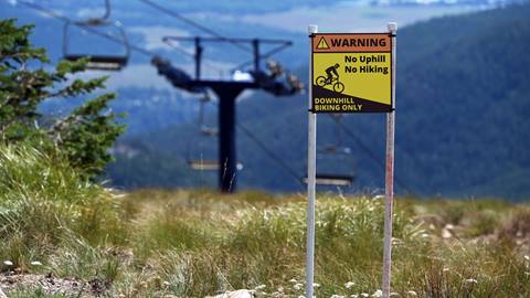 Warning sign at Schweitzer saying 'Downhill Mountain Biking only. No foot traffic."  with view of grass and lift tower. 