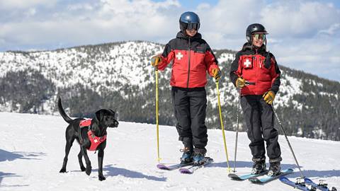 Two Schweitzer ski patrol standing with their avy dog. 