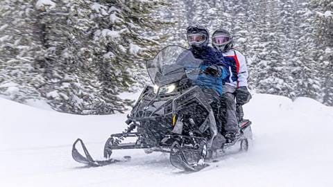 two people riding snowmobile in snowy forest