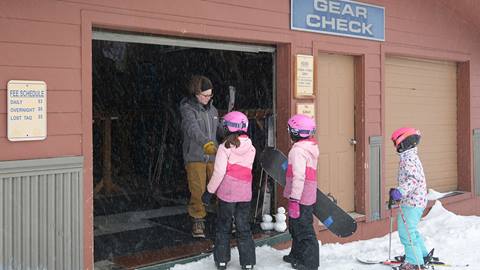 employee helping three young people store their gear in gear check.