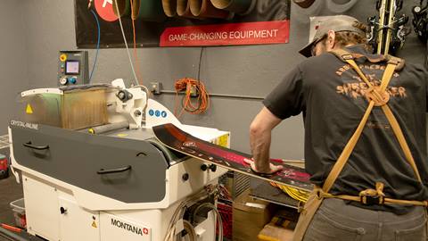 Staff member tuning a snowboard on a machine.