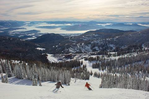 Two people skiing down with the lake in the background