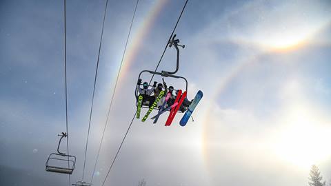 Happy skiers on chairlift with sun halo in the background