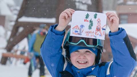 young child smiling and holding up a picture they drew