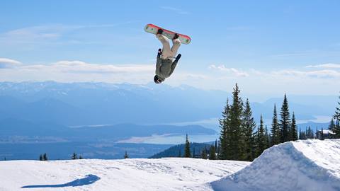 Snowboarder throwing a back flip off a jump at Schweitzer  on a sunny day with the lake in the background