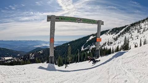 Entrance arch at the top of Stomping Grounds Terrain Park with snowboarders riding through